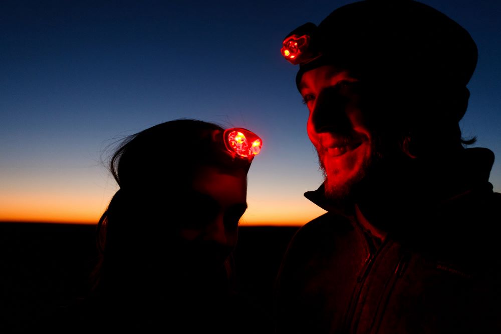two people with red light head lamps at night
